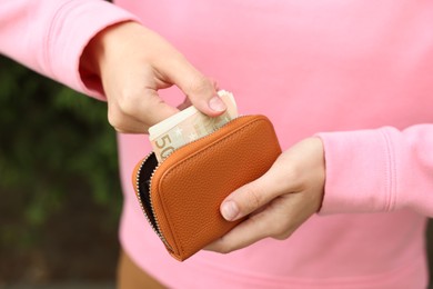 Photo of Woman putting money into wallet outdoors, closeup