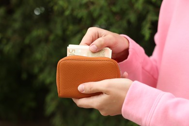 Photo of Woman putting money into wallet outdoors, closeup