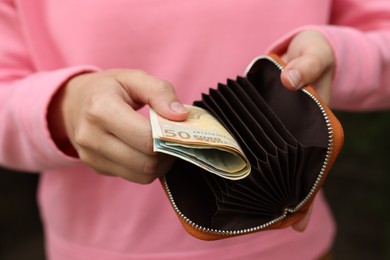 Photo of Woman putting money into wallet outdoors, closeup