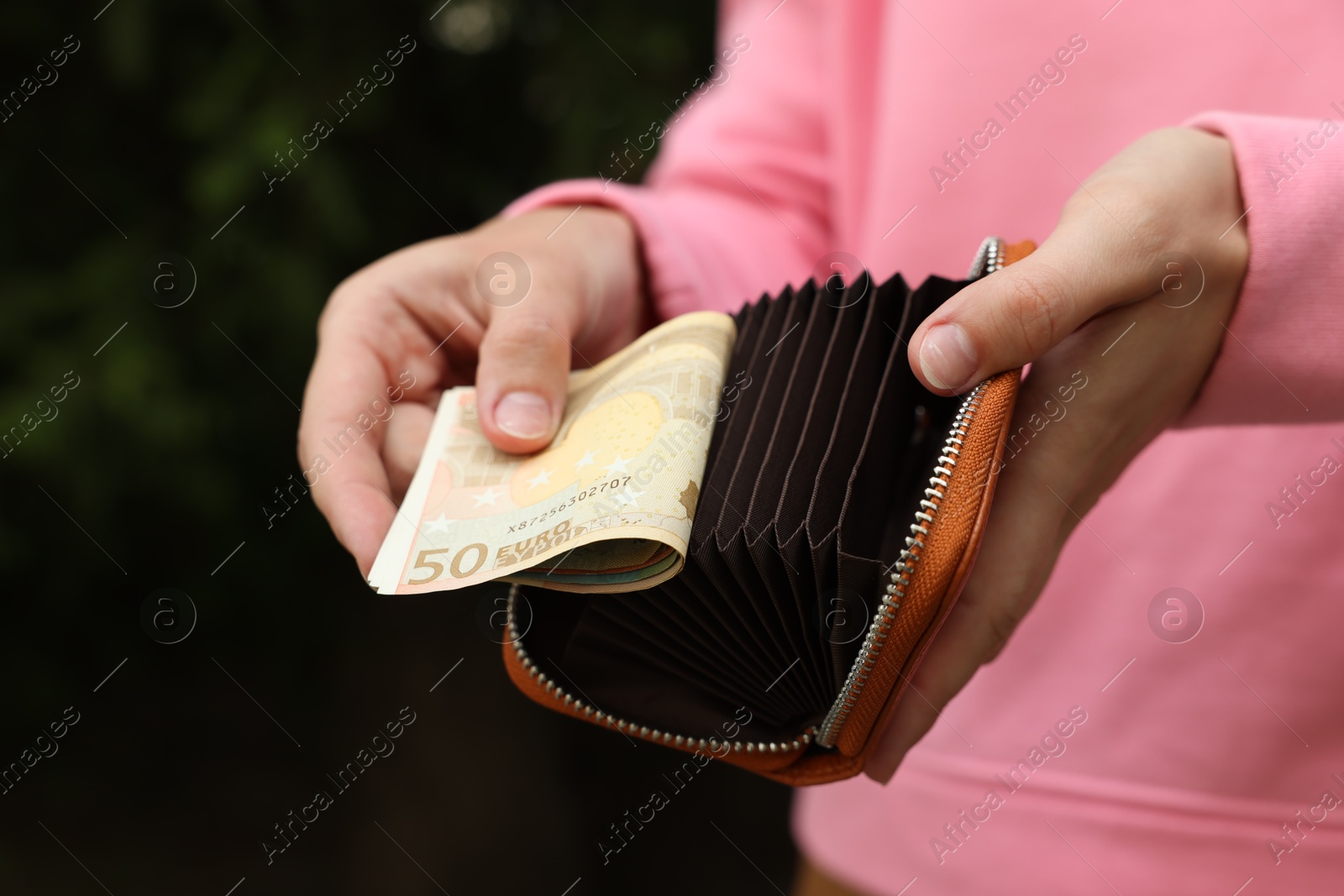 Woman putting money into wallet outdoors, closeup Photo of Woman putting money into wallet outdoors, closeup