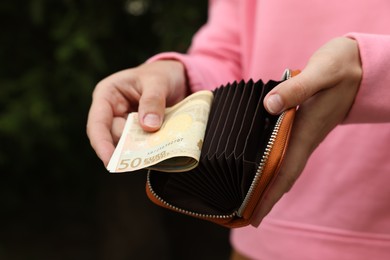 Photo of Woman putting money into wallet outdoors, closeup