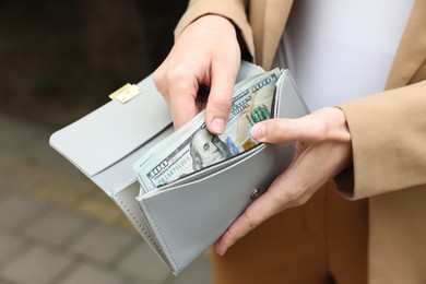 Photo of Woman putting money into wallet outdoors, closeup