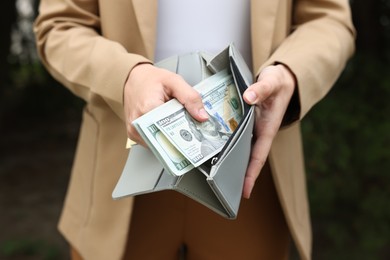 Photo of Woman putting money into wallet outdoors, closeup