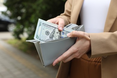 Photo of Woman putting money into wallet outdoors, closeup