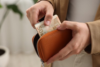 Photo of Woman putting money into wallet indoors, closeup