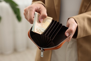 Photo of Woman putting money into wallet indoors, closeup