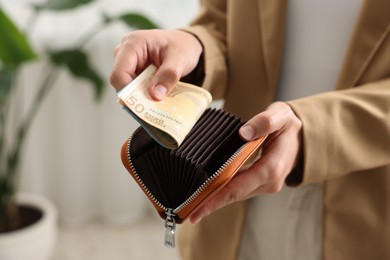 Photo of Woman putting money into wallet indoors, closeup