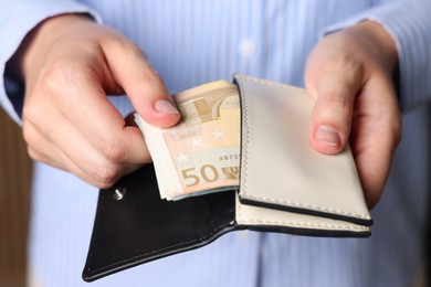 Photo of Woman putting money into wallet indoors, closeup