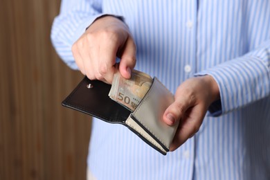 Photo of Woman putting money into wallet indoors, closeup