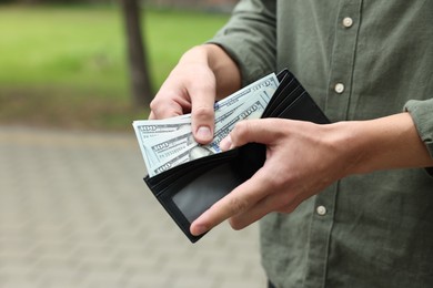 Photo of Man putting money into wallet outdoors, closeup