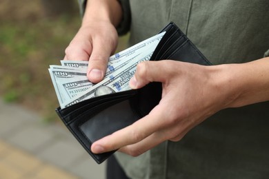 Photo of Man putting money into wallet outdoors, closeup