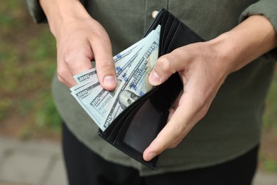 Photo of Man putting money into wallet outdoors, closeup