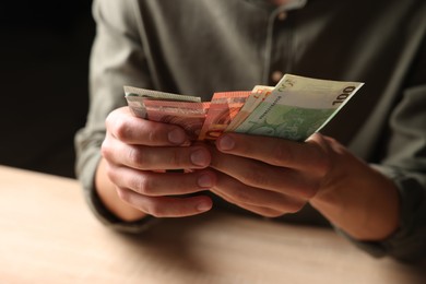 Photo of Man counting money at wooden table, closeup