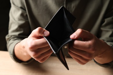 Photo of Man with empty wallet at wooden table, closeup