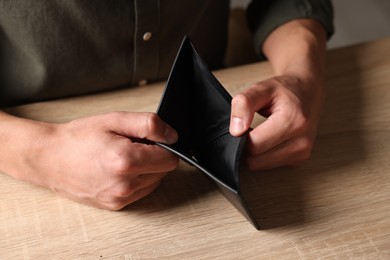 Photo of Man with empty wallet at wooden table, closeup