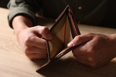 Photo of Man with empty wallet at wooden table, closeup
