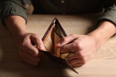 Photo of Man with empty wallet at wooden table, closeup