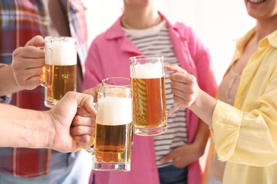 Photo of Friends clinking glass mugs of beer indoors, closeup