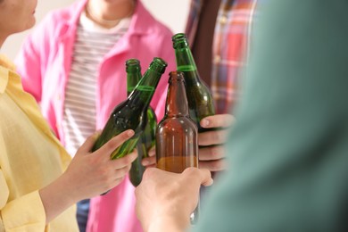 Photo of Friends clinking bottles of beer indoors, closeup