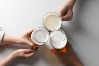 Photo of Friends clinking glasses of beer at white table, top view