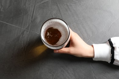 Photo of Woman with glass of beer at grey table, top view