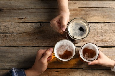 Photo of Friends with glasses of beer at wooden table, top view. Space for text