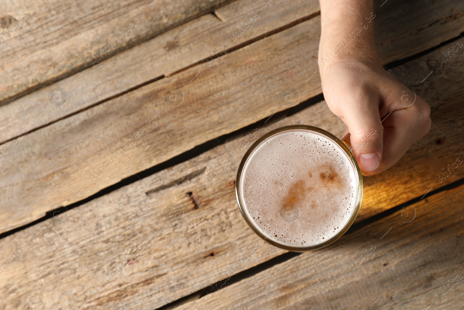 Photo of Man with glass mug of beer at wooden table, top view. Space for text