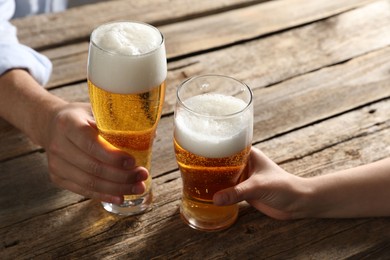 Photo of Friends with glasses of beer at wooden table, closeup