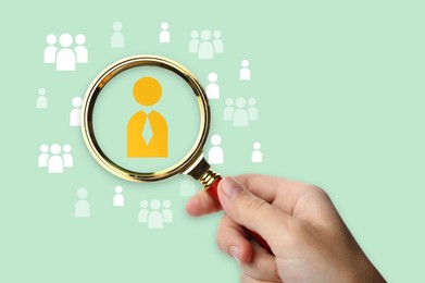 Image of Targeting. Woman holding magnifying glass over human icons against light green background, closeup