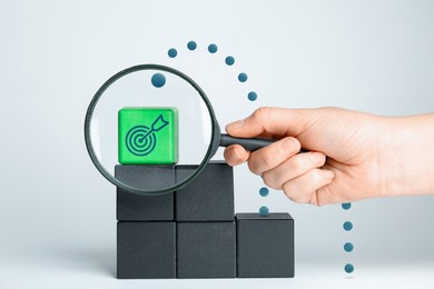 Image of Targeting, business strategy, planning. Woman holding magnifying glass in front of green cube with bullseye icon, closeup