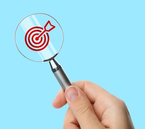 Image of Targeting. Woman holding magnifying glass with bullseye icon inside against light blue background, closeup