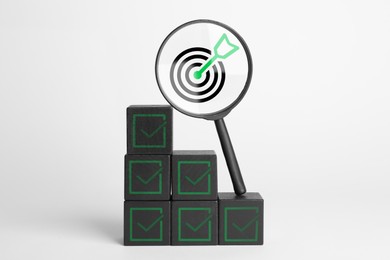 Image of Targeting, business strategy, planning. Black cubes with check marks and magnifying glass with bullseye icon inside against white background