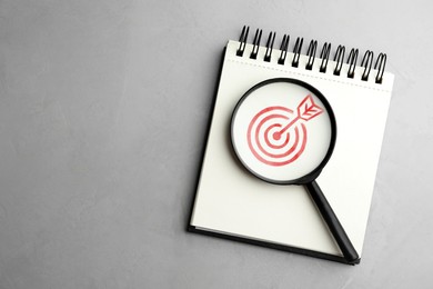 Image of Targeting. Magnifying glass on notebook with bullseye on light grey background, top view