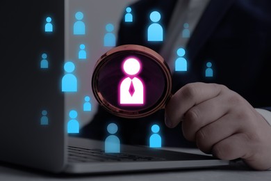 Image of Targeting. Man holding magnifying glass with human icon inside over laptop, closeup