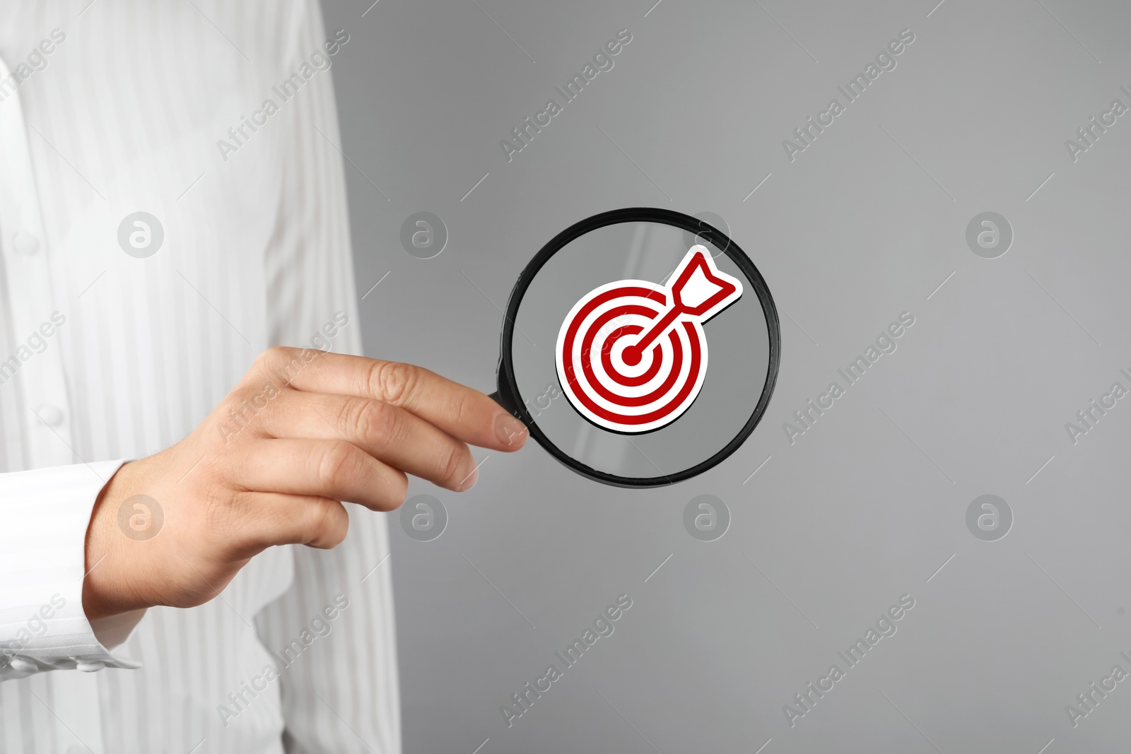 Image of Targeting. Woman holding magnifying glass with bullseye icon inside against grey background, closeup