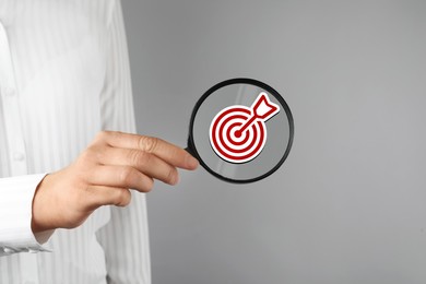 Image of Targeting. Woman holding magnifying glass with bullseye icon inside against grey background, closeup