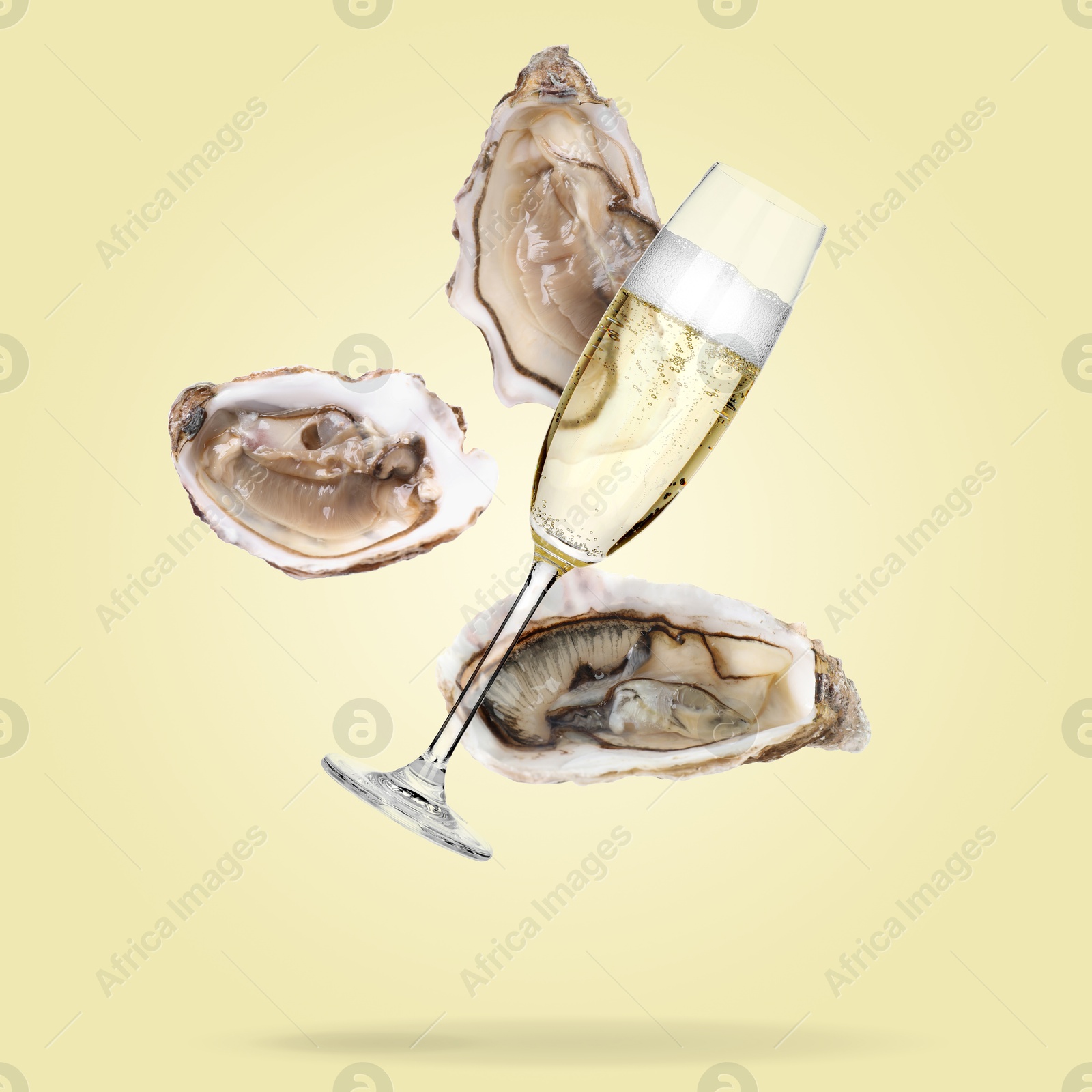 Image of Sparkling wine in glass and fresh oysters falling on pale yellow background