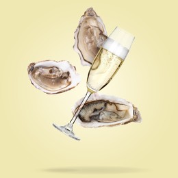Image of Sparkling wine in glass and fresh oysters falling on pale yellow background