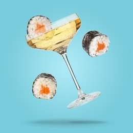 Image of Sparkling wine in glass and sushi rolls falling on light blue background