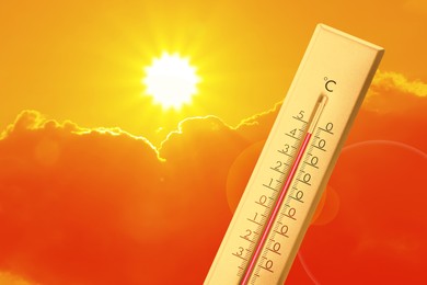 Image of Extremely high temperature on thermometer against orange sky on sunny day. Severely hot summer weather