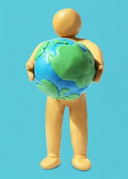 Image of Yellow plasticine human figure holding planet on light blue background
