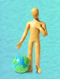 Image of Yellow plasticine human figure with planet on turquoise background