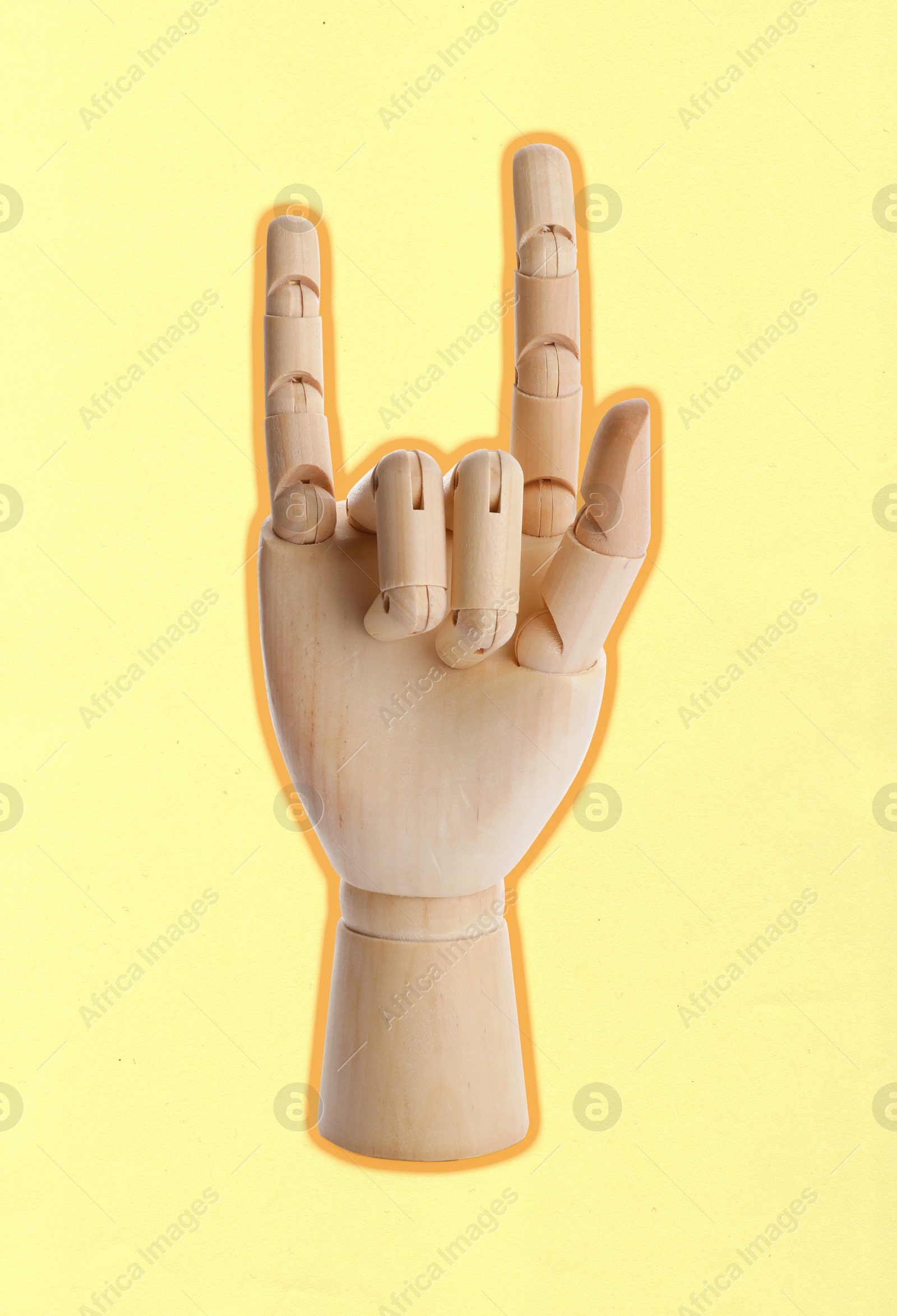 Wooden mannequin hand showing rock gesture on pale yellow background Image of Wooden mannequin hand showing rock gesture on pale yellow background