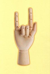 Image of Wooden mannequin hand showing rock gesture on pale yellow background
