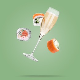 Image of Sparkling wine in glass and sushi rolls falling on light green background