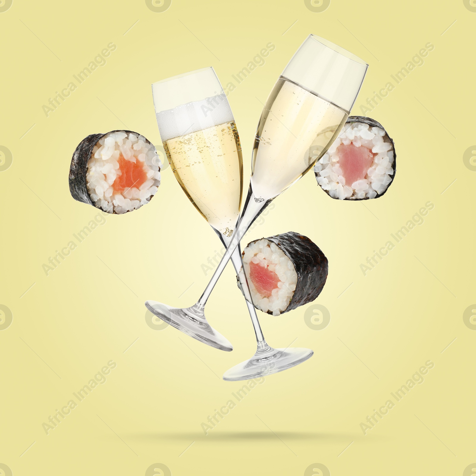 Sparkling wine in glasses and sushi rolls falling on pale yellow background Image of Sparkling wine in glasses and sushi rolls falling on pale yellow background