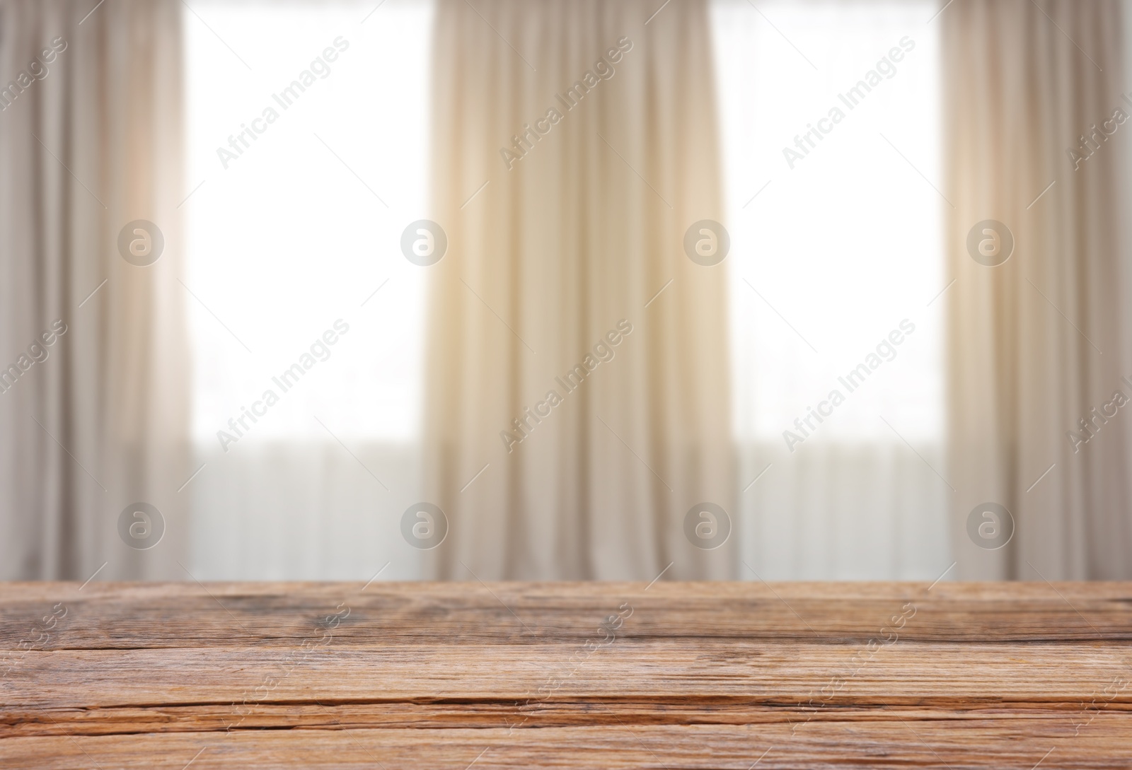 Empty wooden table against windows with curtains in room Image of Empty wooden table against windows with curtains in room