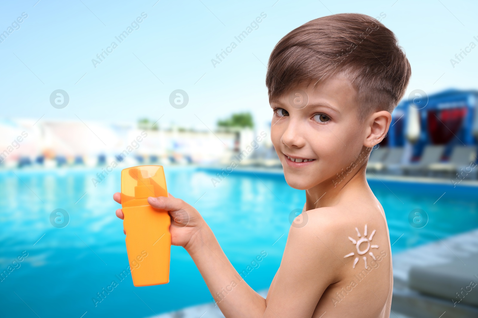 Image of Little boy with bottle of sunscreen by outdoor swimming pool. Sun protection product on his shoulder