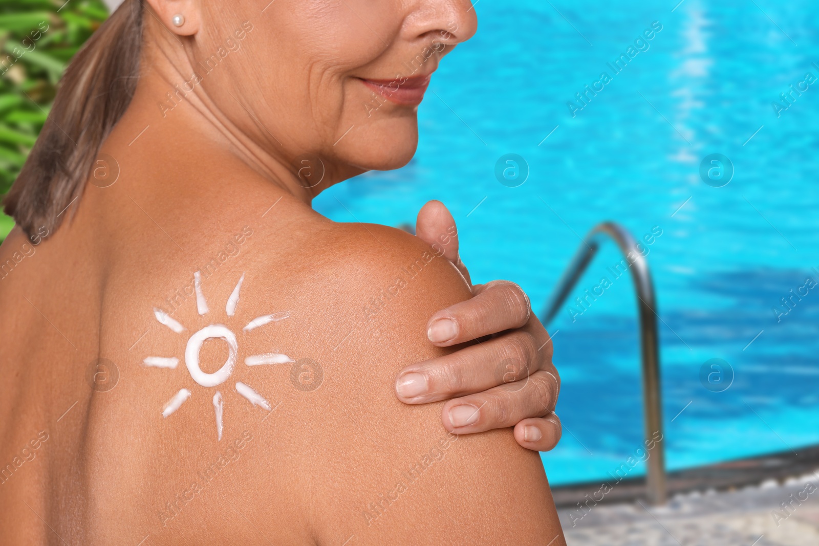 Image of Woman with sun protection product on her shoulder by outdoor swimming pool, closeup