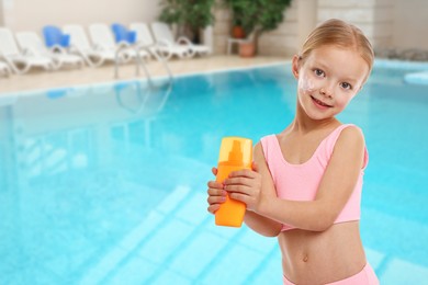 Image of Cute little girl with bottle of sunscreen by outdoor swimming pool. Sun protection product on her cheek